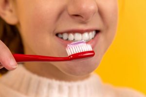 Young woman smiling while brushing teeth with a red toothbrush and fluoride toothpaste