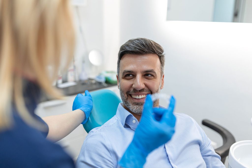 Adult male patient smiling while dentist shows him a clear Invisalign aligner during a consultation